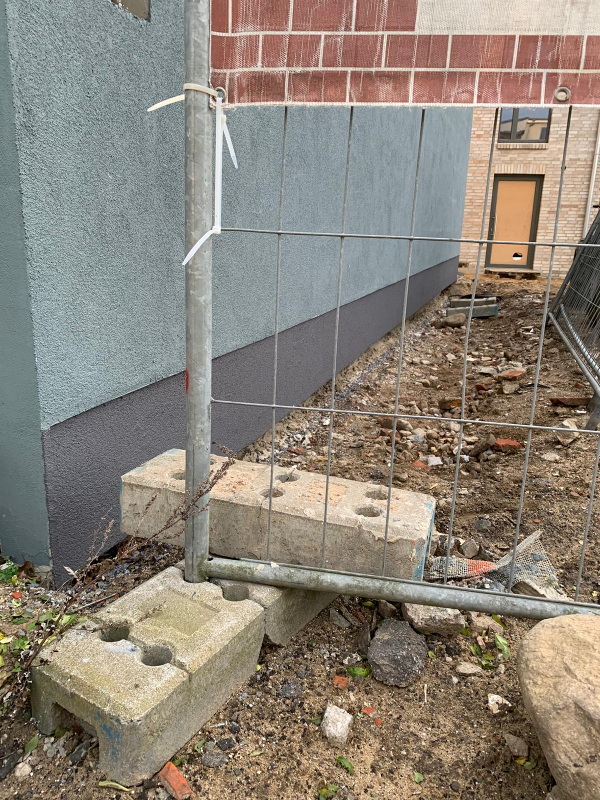 Baustelle mit mobilen Absperrgittern auf Betonsteinfüßen entlang einer frisch verputzten Gebäudefassade