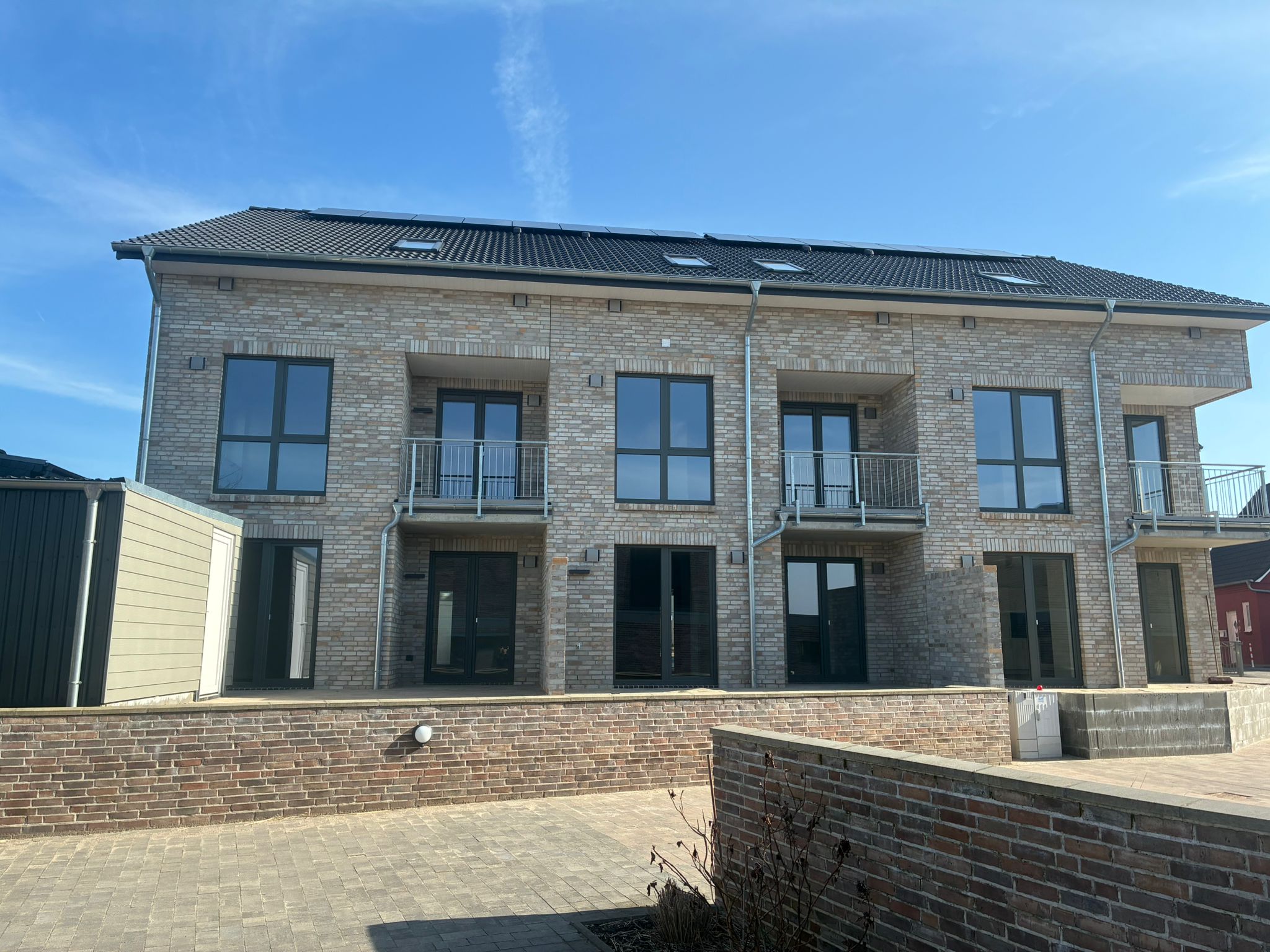Neubau-Mehrfamilienhaus mit heller Klinkerfassade, Balkonen, großen Fenstern und Solaranlage auf dem Dach