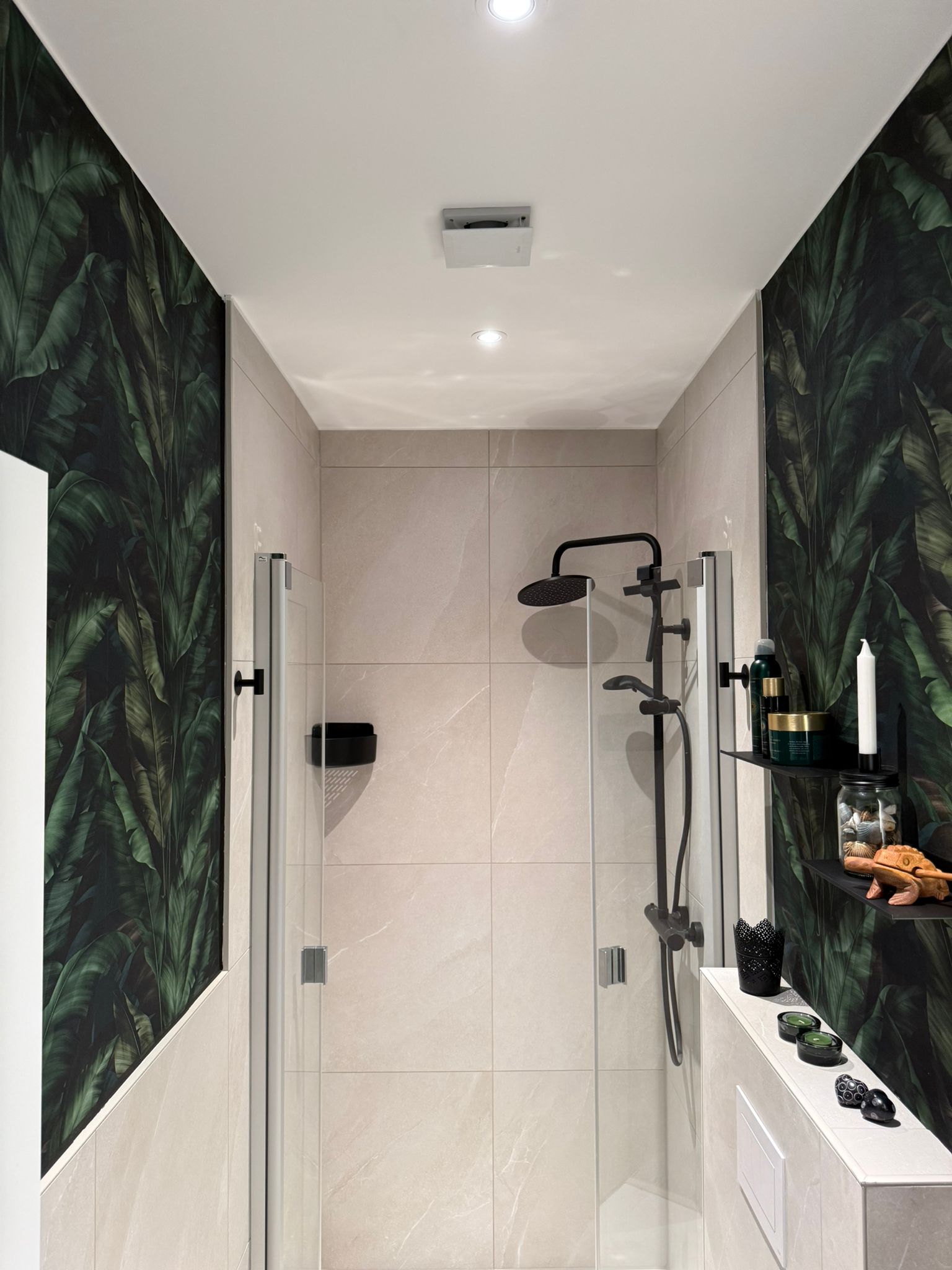 Modernes Badezimmer mit Glasdusche, schwarzen Armaturen, hellen Fliesen und tropischer Blätter-Tapete