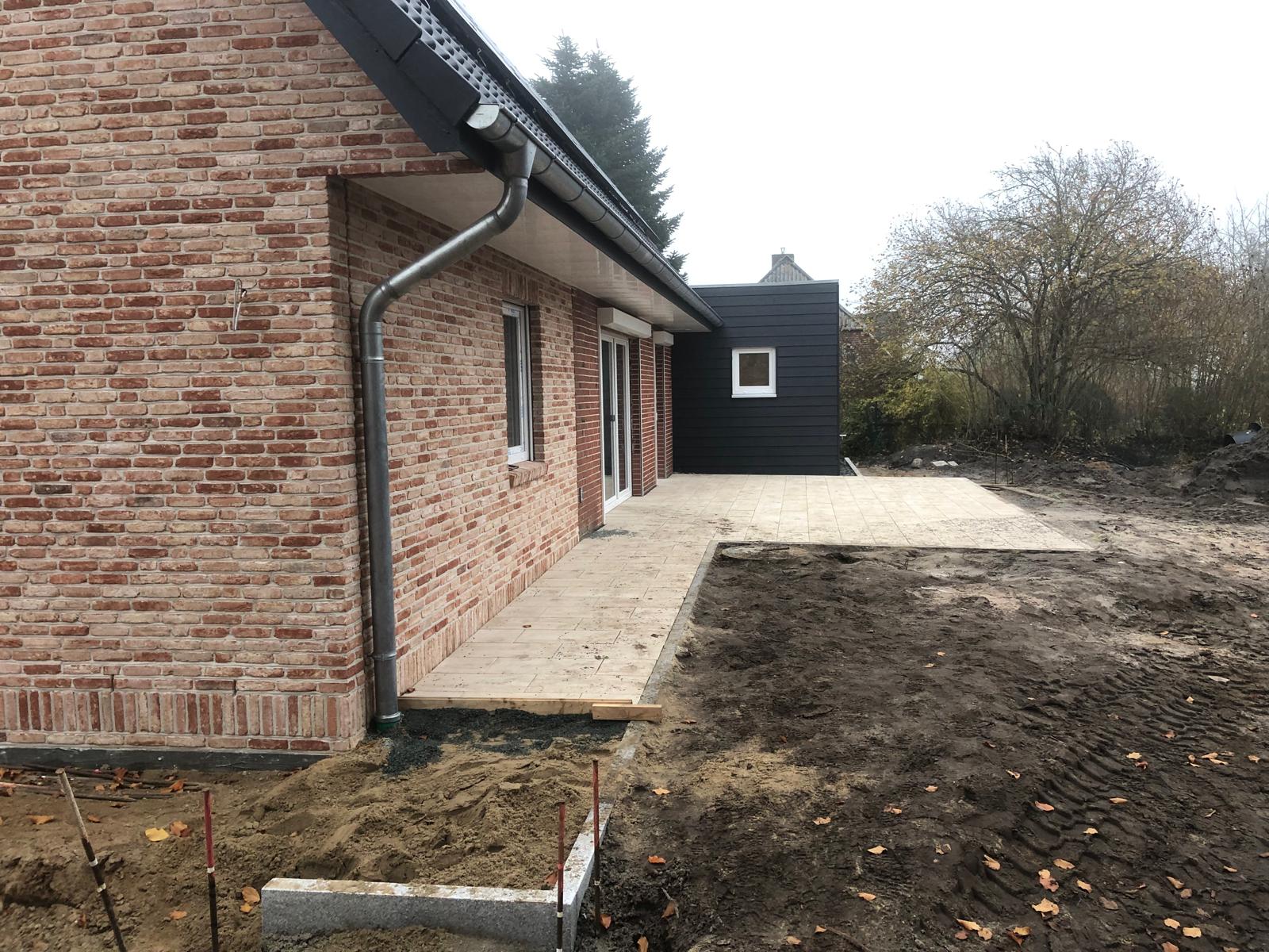 Neubau mit Klinkerfassade und dunklem Anbau, neu verlegte Terrassenplatten, Außenbereich noch im Rohbauzustand