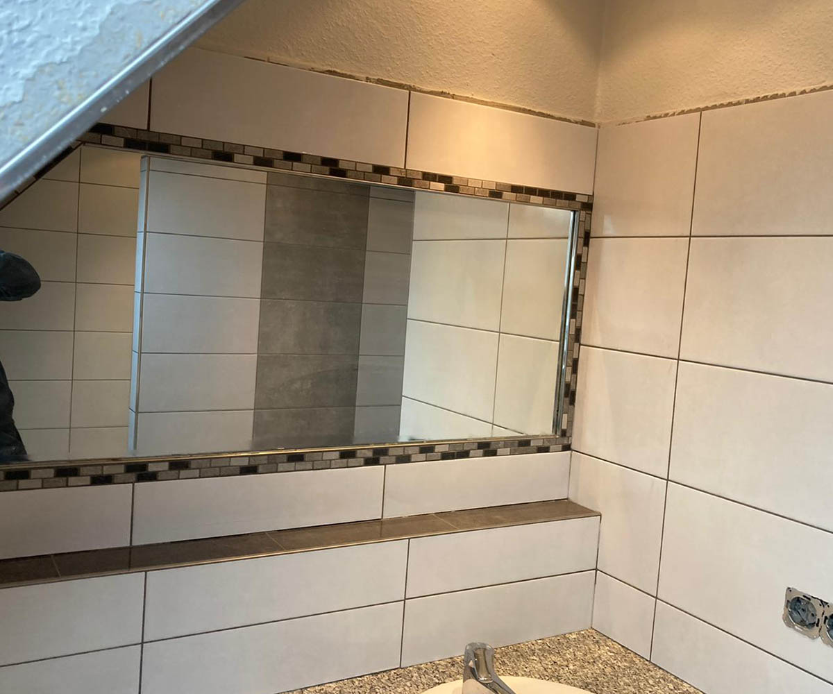 Gefliestes Badezimmer mit großem Wandspiegel, weißen Fliesen und dekorativem Mosaikstreifen als Bordüre