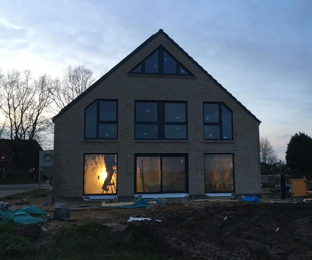 Neubau eines Einfamilienhauses mit Klinkerverkleidung und großen Fensterfronten im Rohbauzustand bei Abenddämmerung