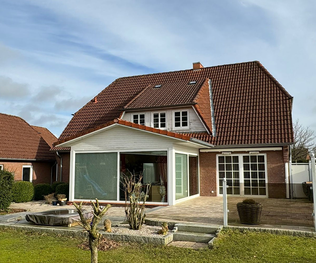 Einfamilienhaus mit rotem Ziegeldach, Wintergarten-Anbau und gepflasterter Terrasse mit Whirlpool im Garten
